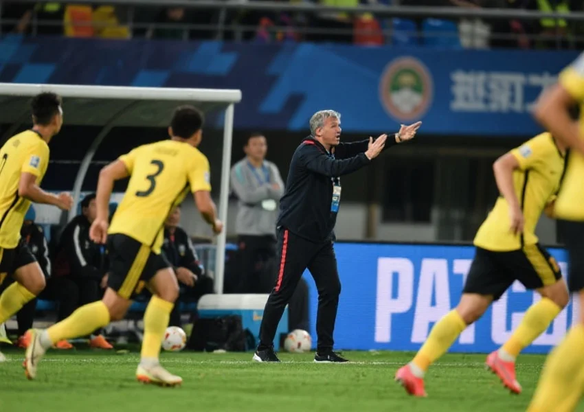 足球教练在场边激烈指挥战术，球员们按指示迅速移动，展现团队协作与战术执行力